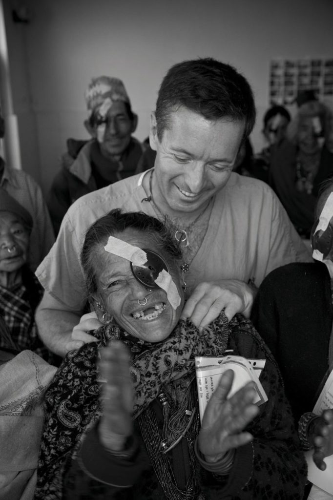 Man standing behind a laughing patient whose left eye is covered with a patch