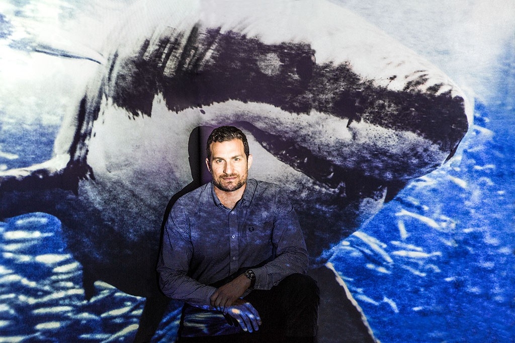 Man sitting in front of a screen with a great white shark projected on it
