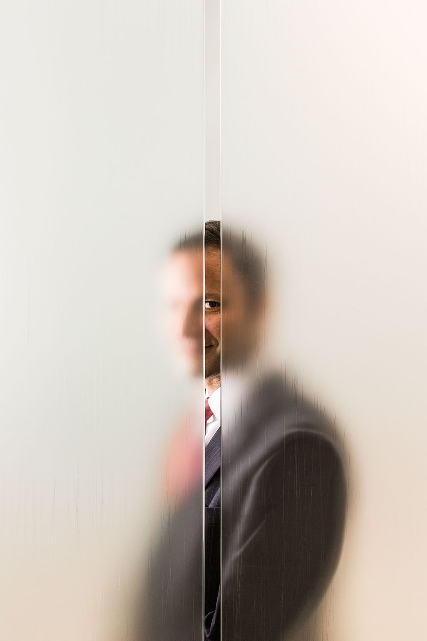 Man standing behind opaque glass looking through a vertical slit