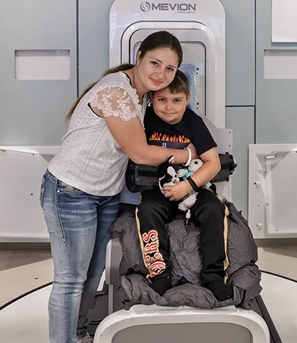 Woman and her child try out the chair of a new proton therapy device that was used to treat the child's rare brain tumor.